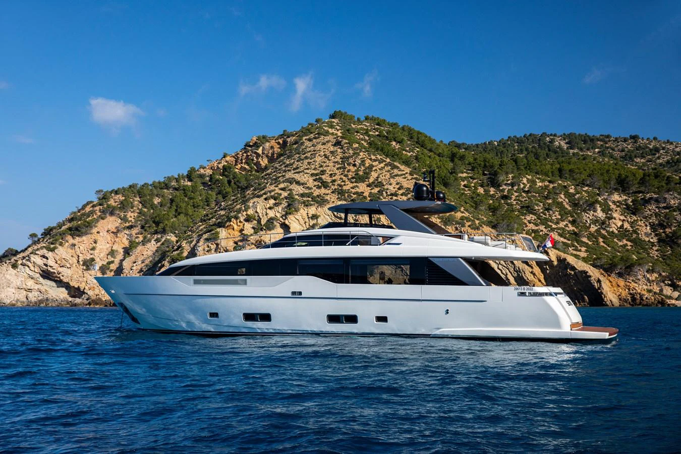 A sleek and modern yacht cruises along a scenic coastline under a clear blue sky. aboard SEVEN Yacht for Sale