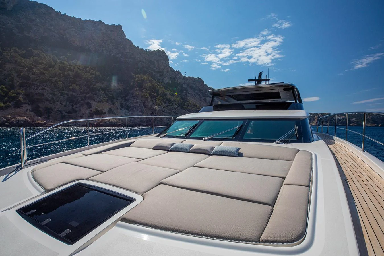 The yacht's foredeck features a spacious sunbathing area with plush cushions, set against a stunning coastal backdrop. aboard SEVEN Yacht for Sale