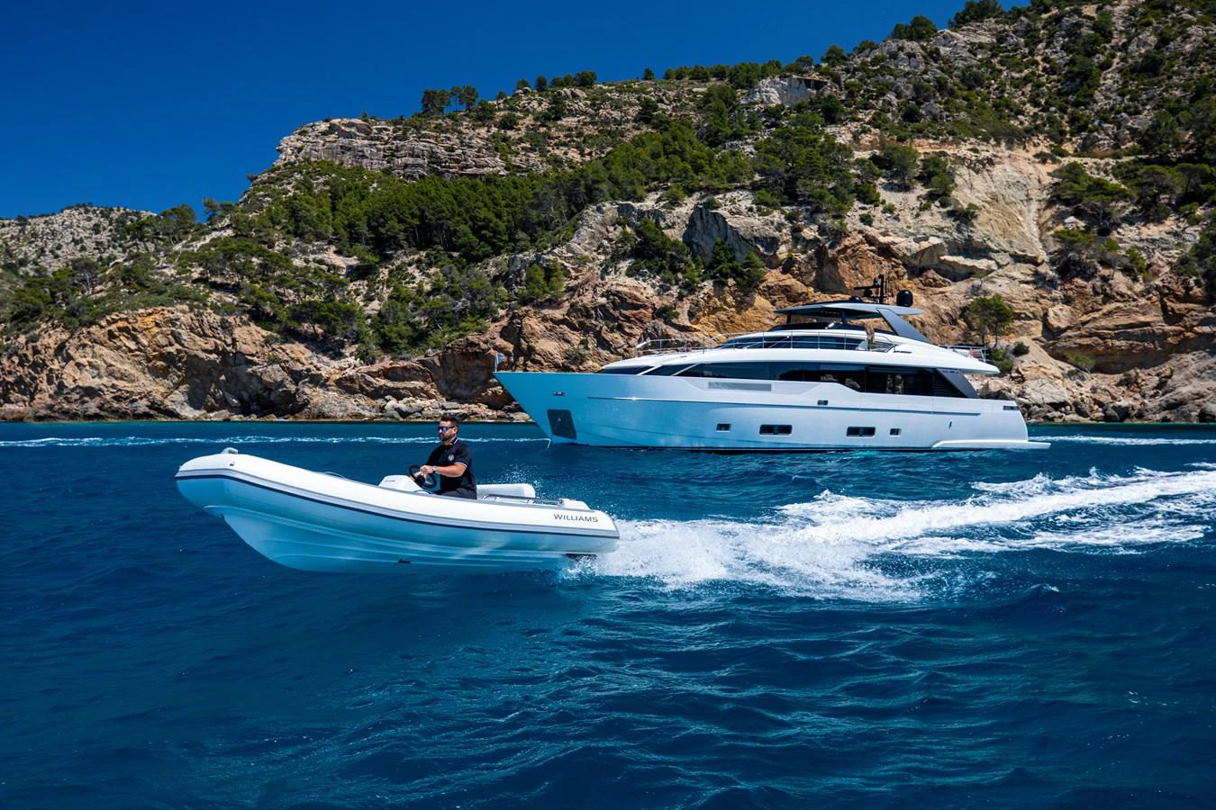 A sleek yacht cruises along a rocky coastline, accompanied by a tender boat. aboard SEVEN Yacht for Sale