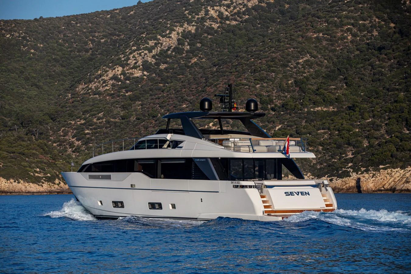 A sleek and modern yacht cruises through calm blue waters with a scenic backdrop. aboard SEVEN Yacht for Sale