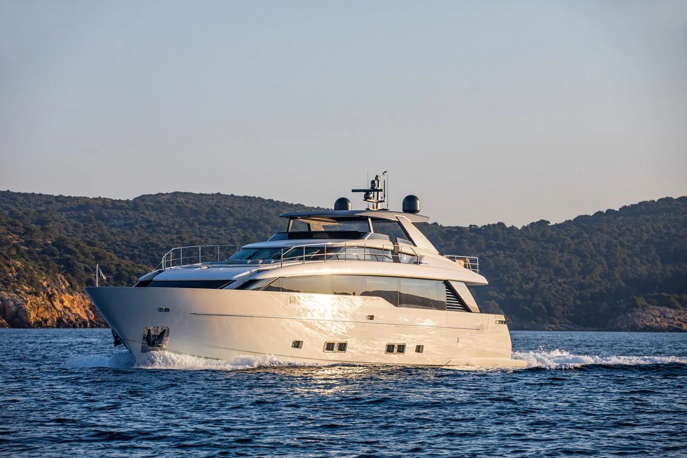 A sleek and modern yacht cruising through calm waters with scenic hills in the background. aboard SEVEN Yacht for Sale