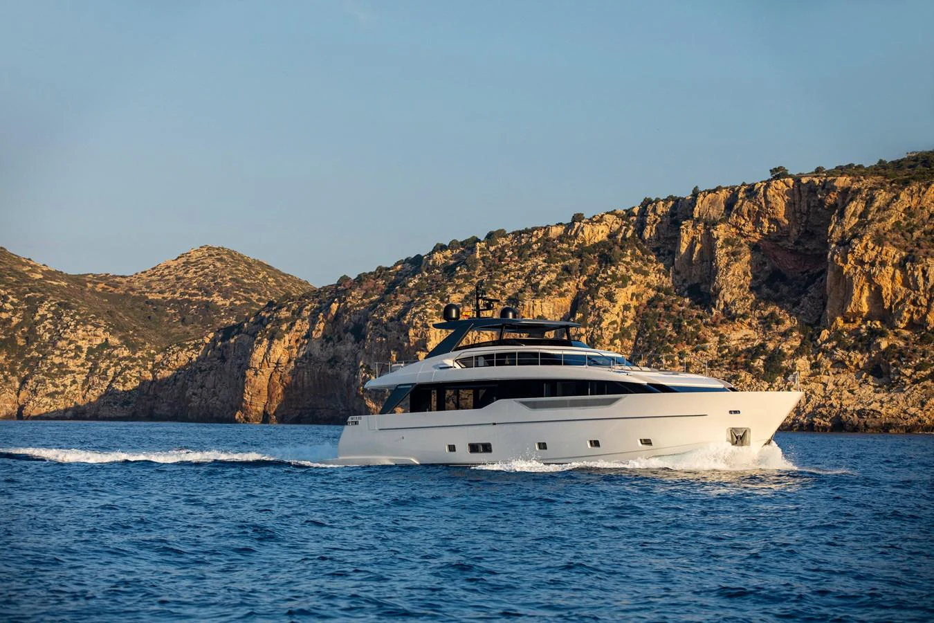 A sleek yacht cruises along a scenic coastline, showcasing its elegant design and modern lines. aboard SEVEN Yacht for Sale