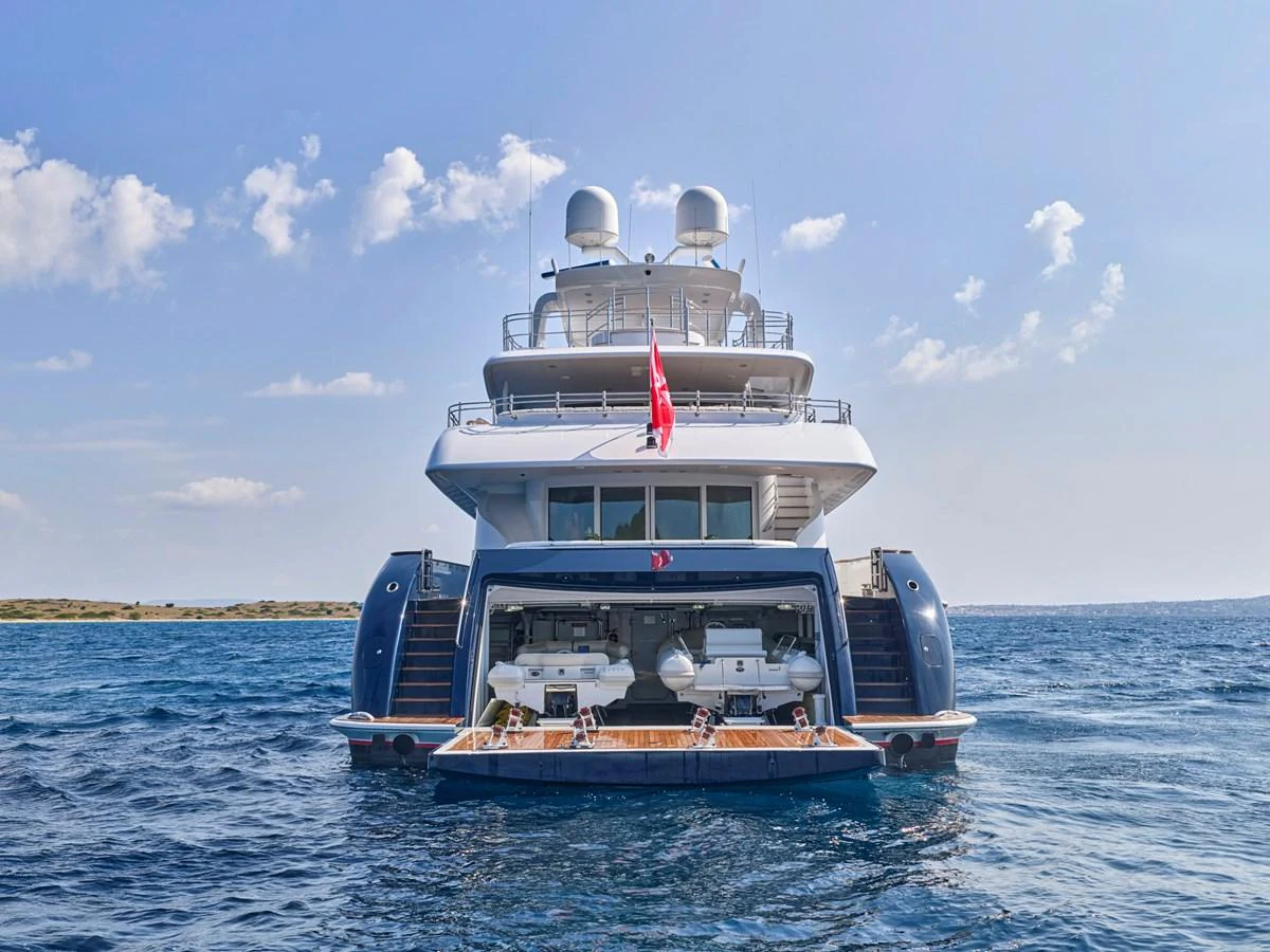 A luxurious yacht is anchored in calm waters, showcasing its spacious aft deck and tender garage. aboard BILMAR Yacht for Sale