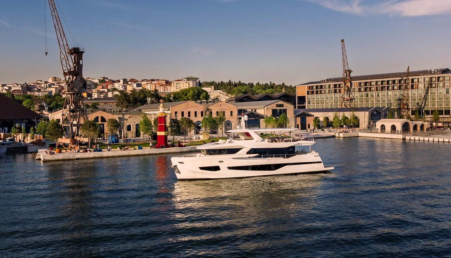 A sleek white yacht cruises gracefully in a bustling harbor with industrial and urban backdrops. aboard NUMARINE 27XP#6 Yacht for Sale
