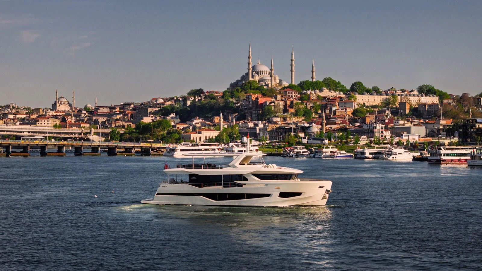 A luxurious yacht cruises gracefully on the water with a picturesque cityscape in the background. aboard NUMARINE 27XP#6 Yacht for Sale