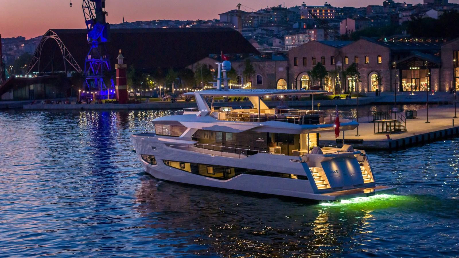 A luxurious yacht is docked at a scenic waterfront during twilight, with city lights reflecting on the water. aboard NUMARINE 27XP#6 Yacht for Sale