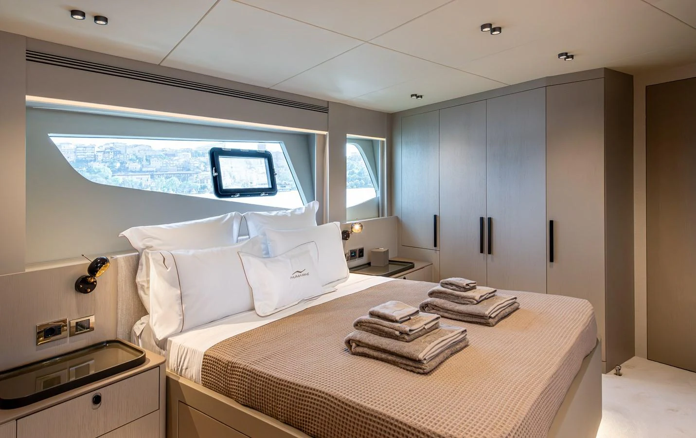 The stateroom features a plush bed with neatly arranged towels and ample natural light from large windows. aboard NUMARINE 27XP#6 Yacht for Sale