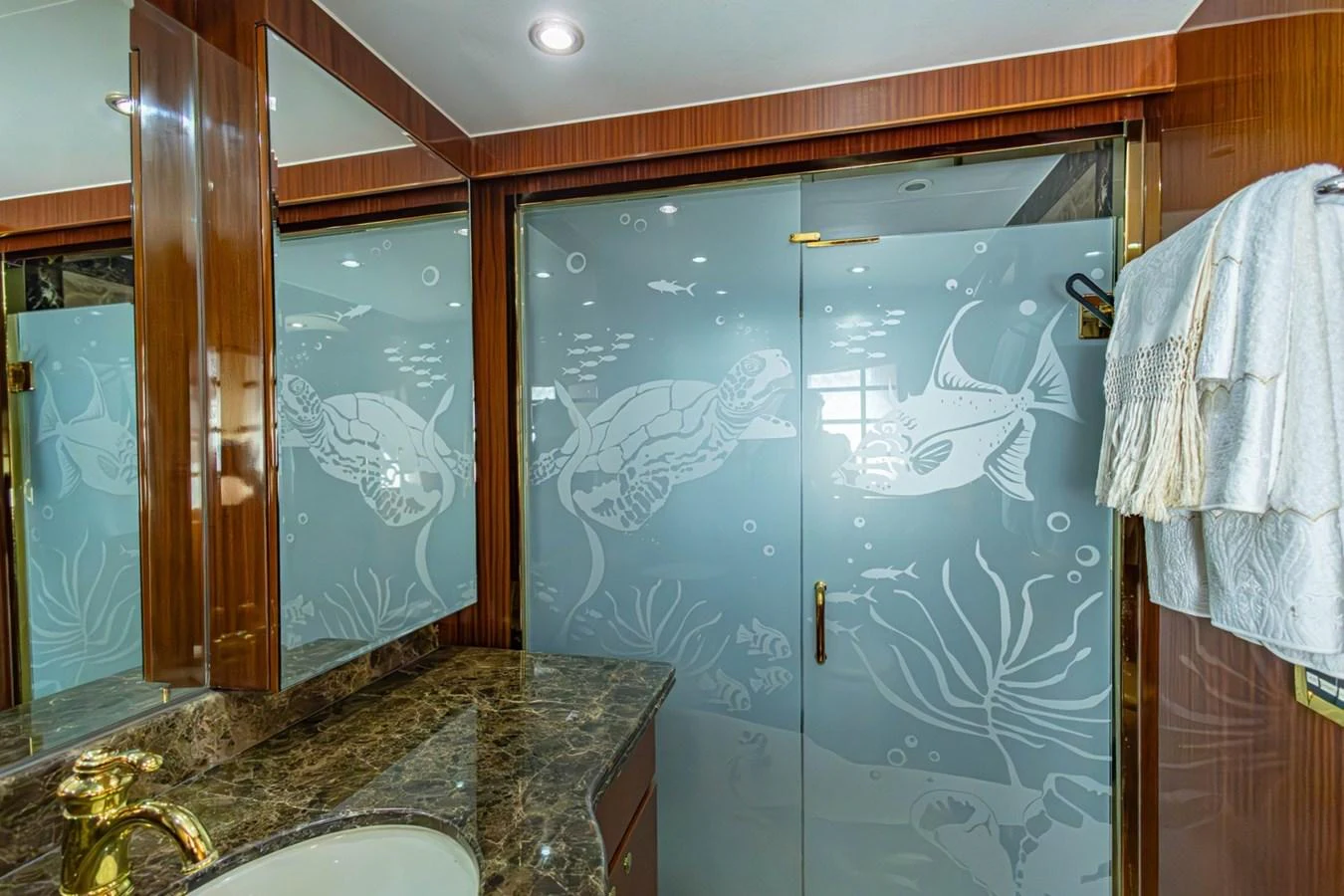The bathroom features elegant etched glass doors with marine life designs and luxurious marble countertops. aboard MY ANGEL Yacht for Sale