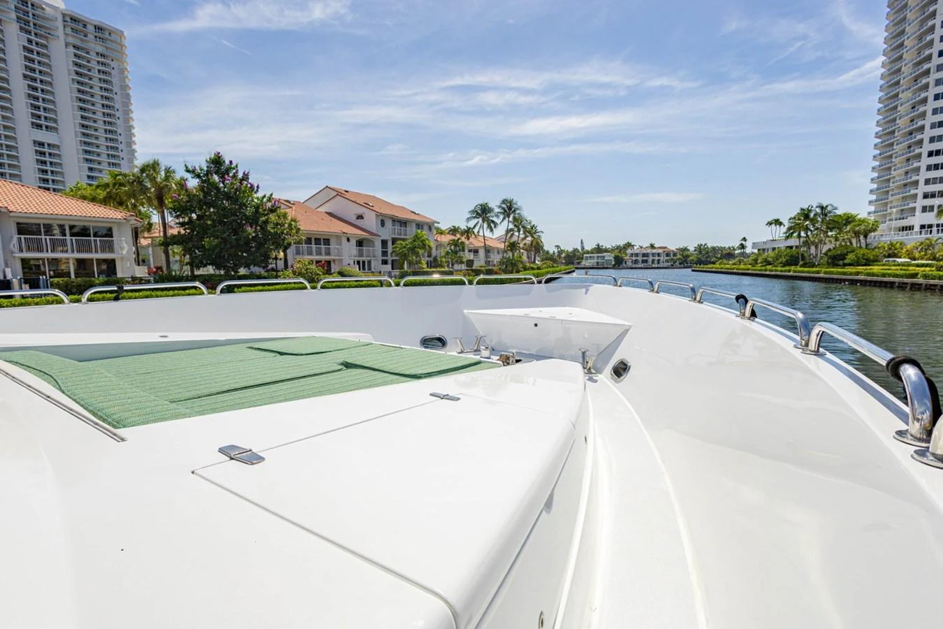 The foredeck of the yacht features a spacious sunbathing area with a green cushion and offers scenic views of the surrounding waterway and buildings. aboard MY ANGEL Yacht for Sale