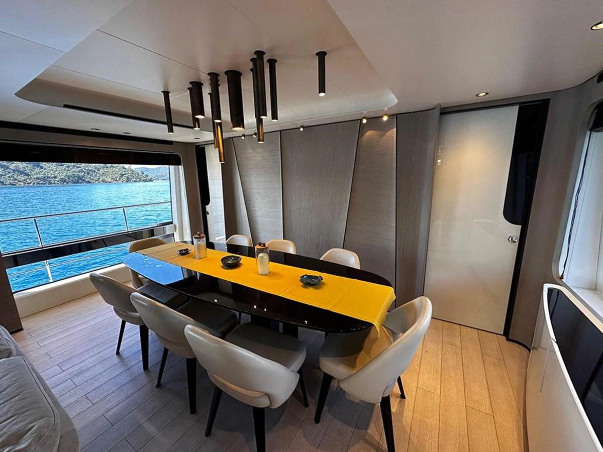 The yacht's dining area features a sleek, modern design with a large table and comfortable seating, complemented by a scenic view through the window. aboard ALEX10 Yacht for Sale