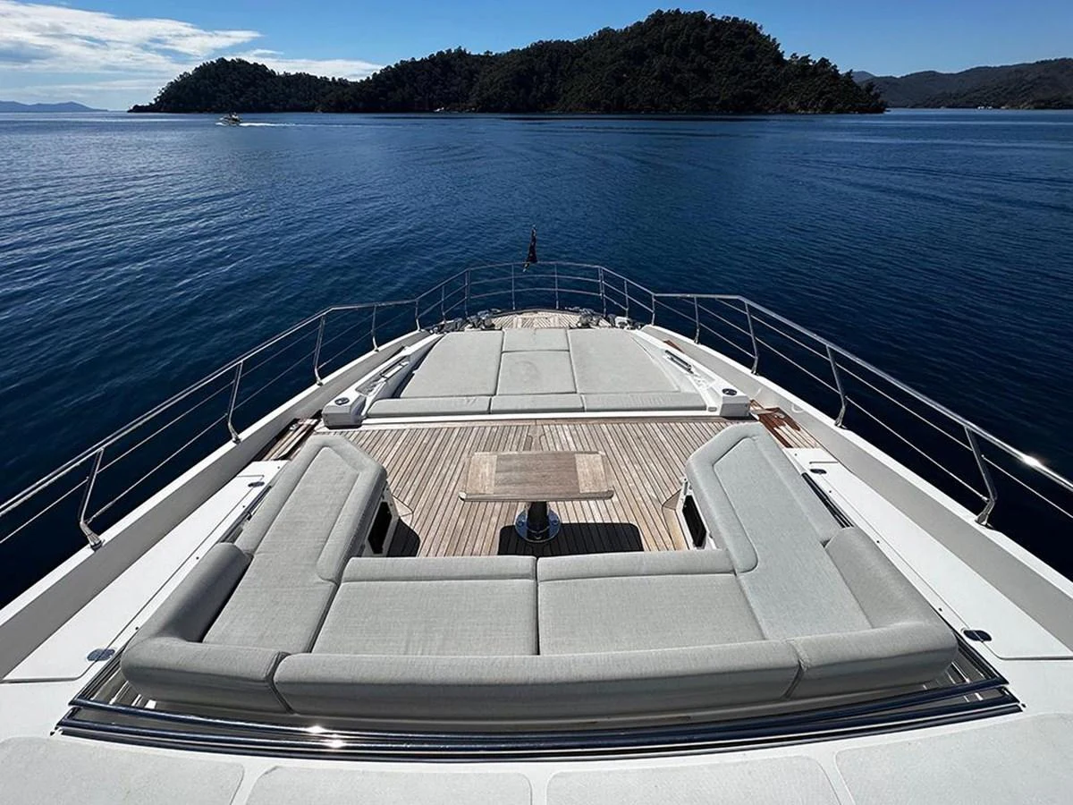 The yacht's foredeck features a spacious sunbathing area with plush seating and a central table, set against a serene ocean backdrop. aboard ALEX10 Yacht for Sale