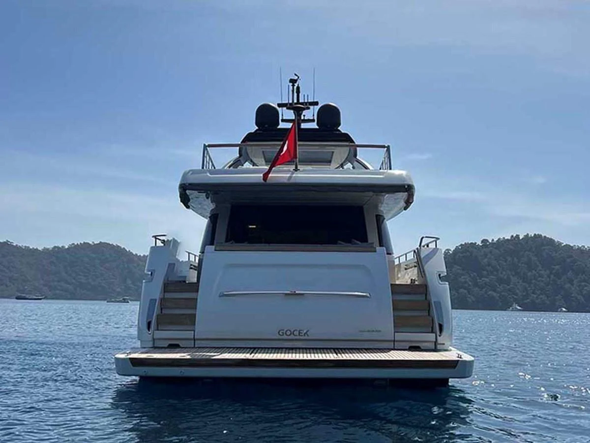 A sleek yacht is anchored on calm waters with a scenic backdrop of lush hills. aboard LA ISLA Yacht for Sale