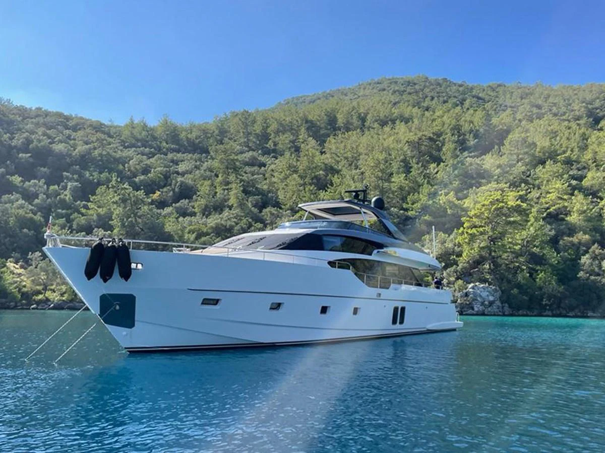A sleek and modern yacht is anchored in a serene, turquoise bay surrounded by lush greenery. aboard LA ISLA Yacht for Sale