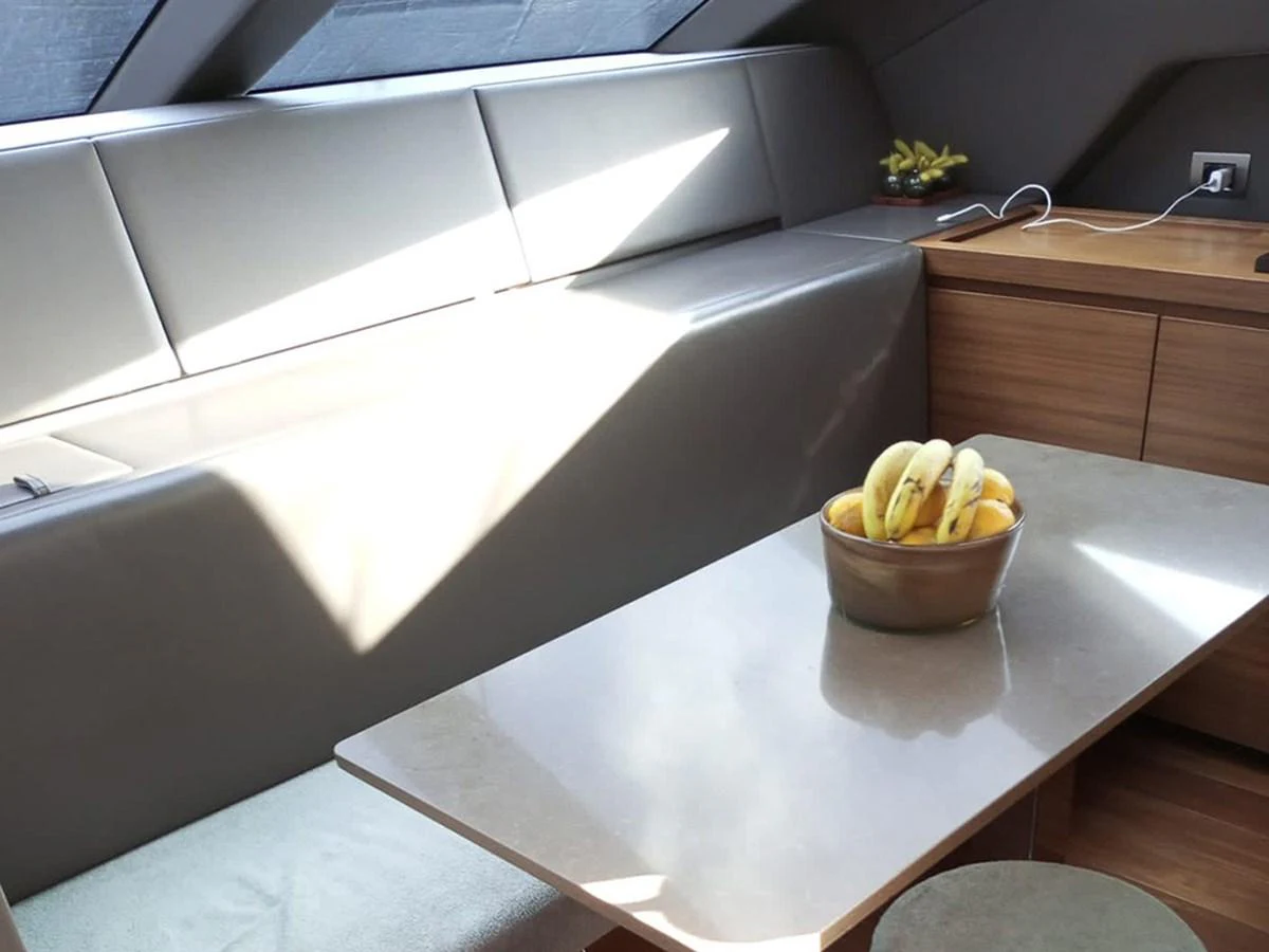 The yacht's salon features a sleek, modern seating area with a table and a bowl of fruit, bathed in natural light. aboard LA ISLA Yacht for Sale