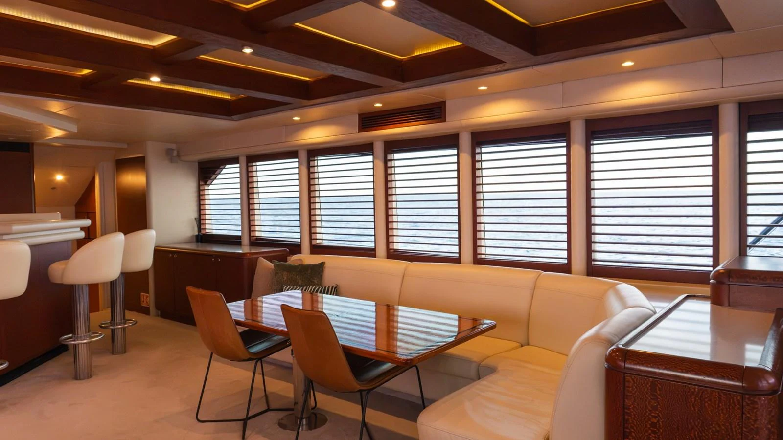 The salon features a spacious seating area with a dining table and bar stools, illuminated by warm lighting. aboard AUSSIE RULES Yacht for Sale