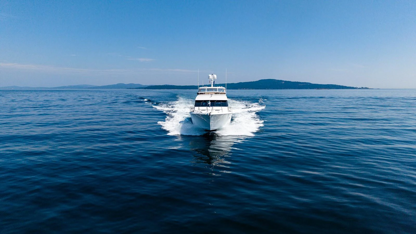 A sleek yacht cruises forward on calm, open waters under a clear blue sky. aboard DAWN TRADER VII Yacht for Sale