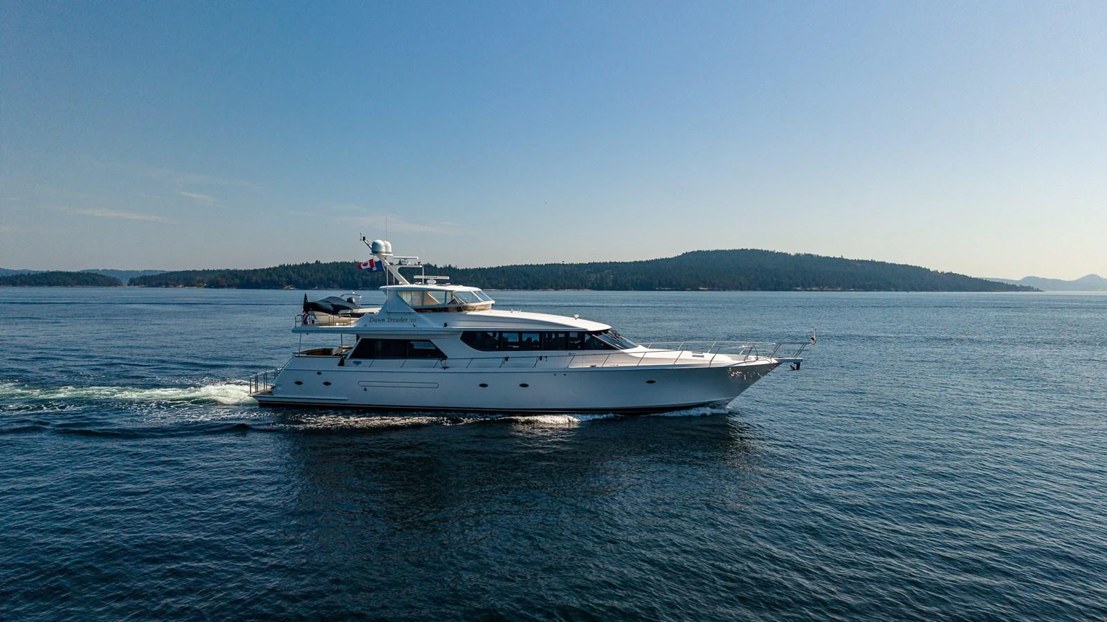 A sleek yacht cruises through calm waters with a scenic backdrop of distant islands. aboard DAWN TRADER VII Yacht for Sale