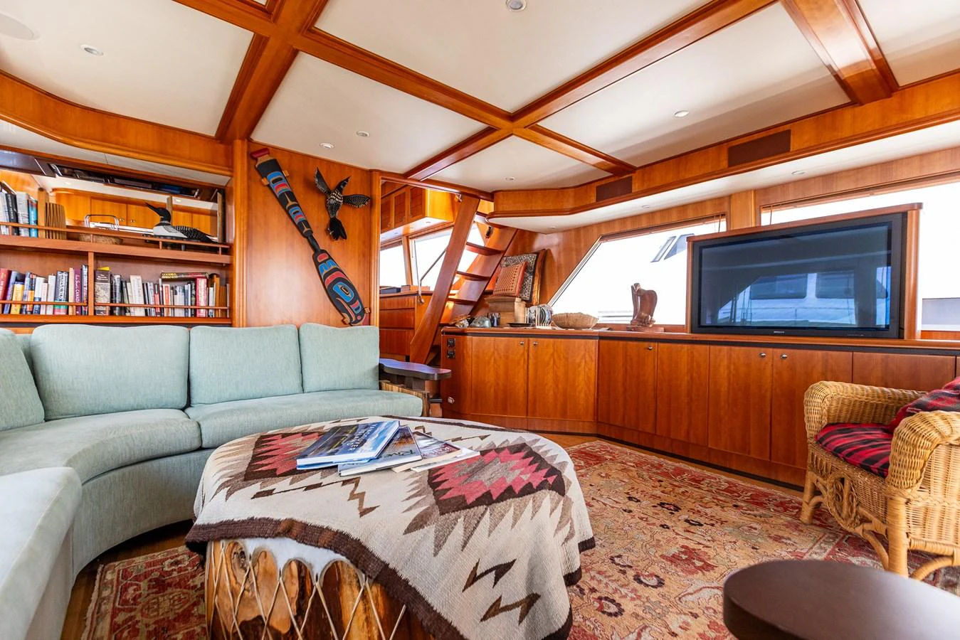 The yacht's salon features a cozy seating area with a large sofa, a flat-screen TV, and a well-stocked bookshelf, all accented by warm wooden finishes. aboard DAWN TRADER VII Yacht for Sale