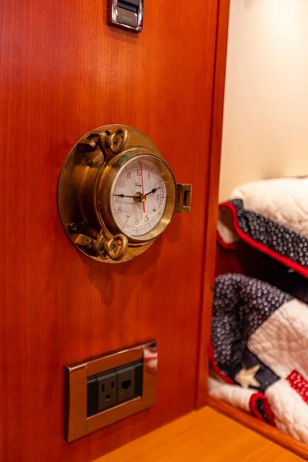 A close-up of a nautical clock mounted on a wooden wall, with a glimpse of a cozy, quilted blanket nearby. aboard DAWN TRADER VII Yacht for Sale
