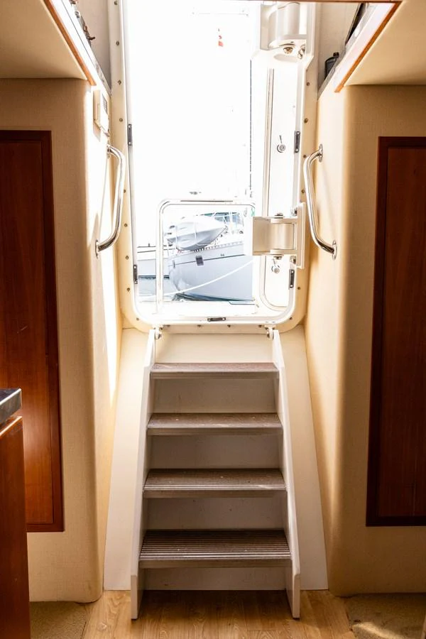 A well-lit interior staircase leads up to an exterior door, showcasing a glimpse of the outside. aboard DAWN TRADER VII Yacht for Sale