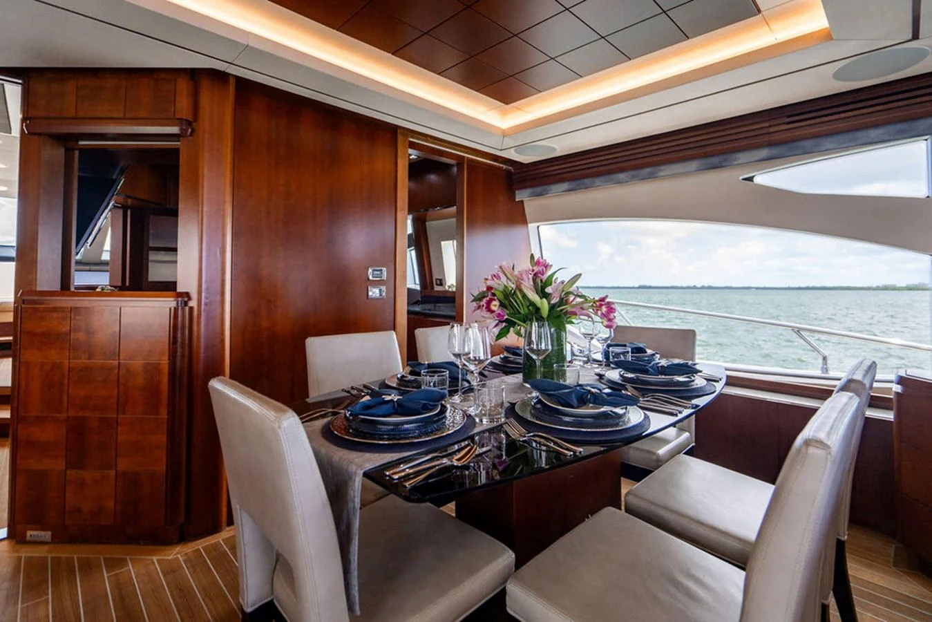 The yacht's dining area features a beautifully set table with a view of the water through large windows. aboard BEAUTIFUL M Yacht for Sale