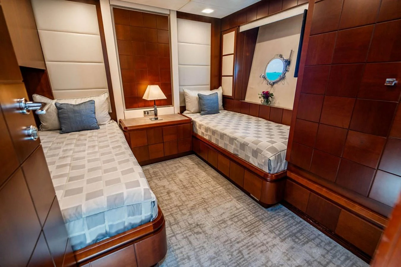This cozy guest stateroom features twin beds, warm wood paneling, and a porthole window. aboard BEAUTIFUL M Yacht for Sale