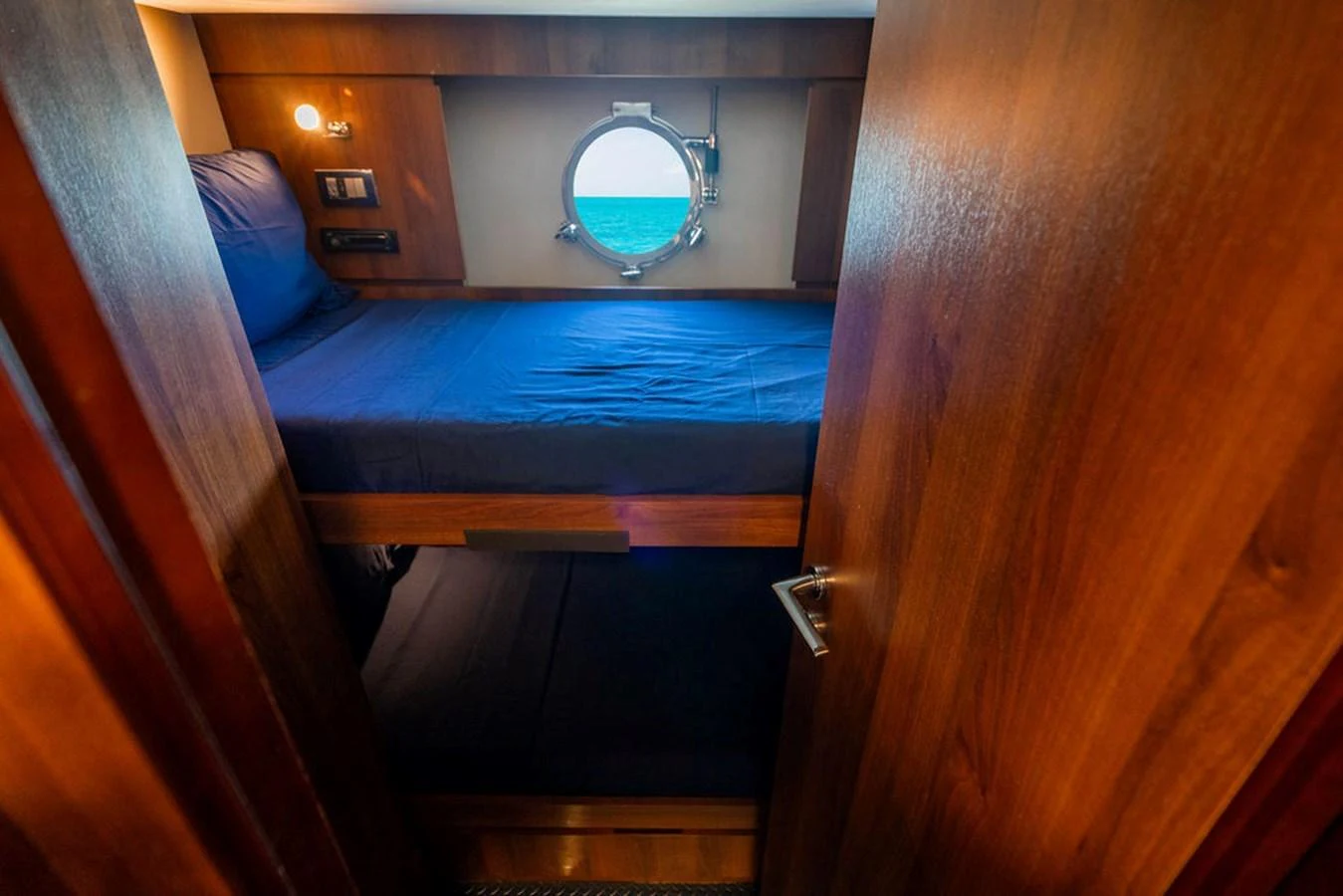 A cozy cabin with wooden finishes and a round porthole offering a view of the sea. aboard BEAUTIFUL M Yacht for Sale