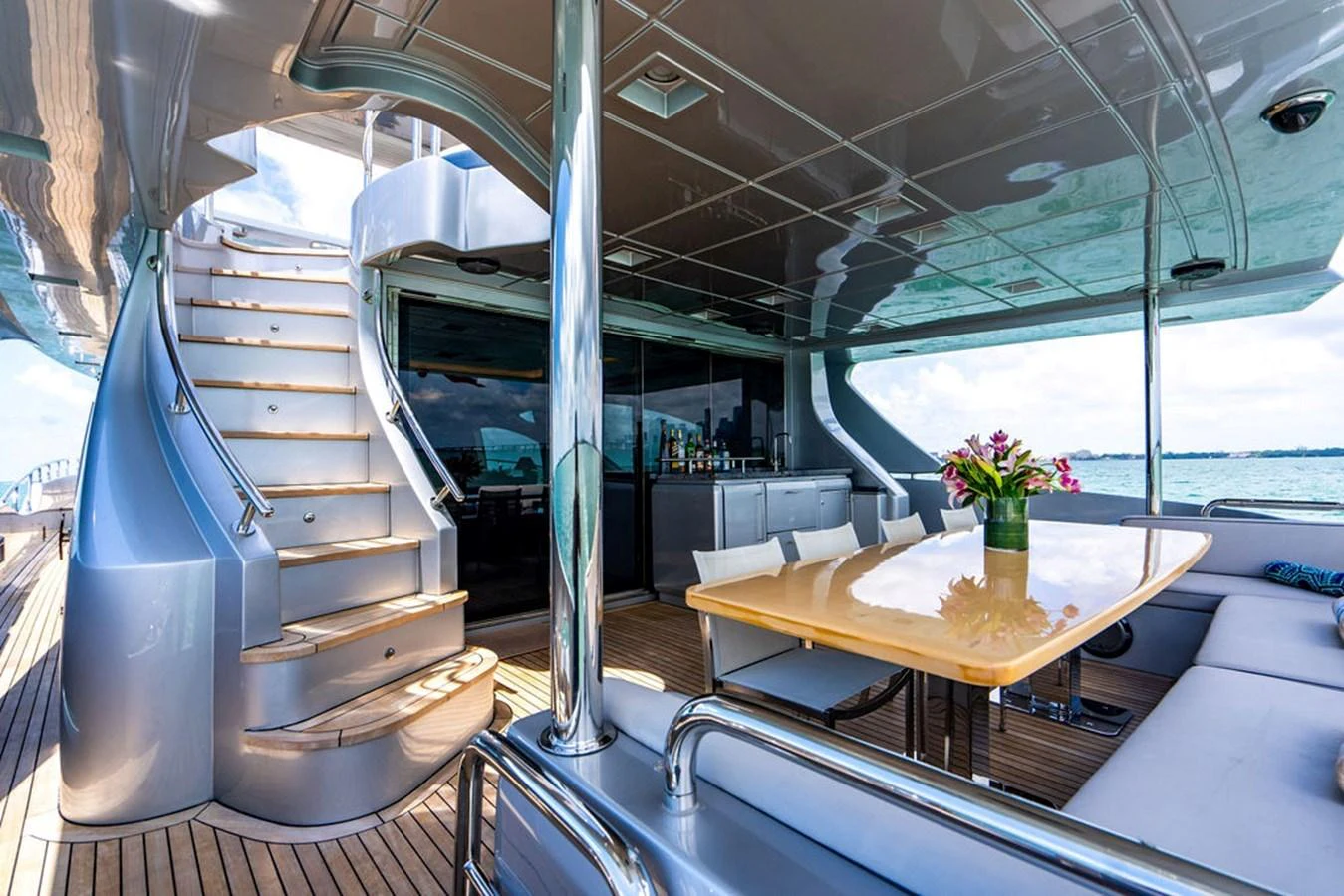 The aft deck features a stylish dining area with a polished table and comfortable seating, complemented by a sleek staircase leading to the upper deck. aboard BEAUTIFUL M Yacht for Sale