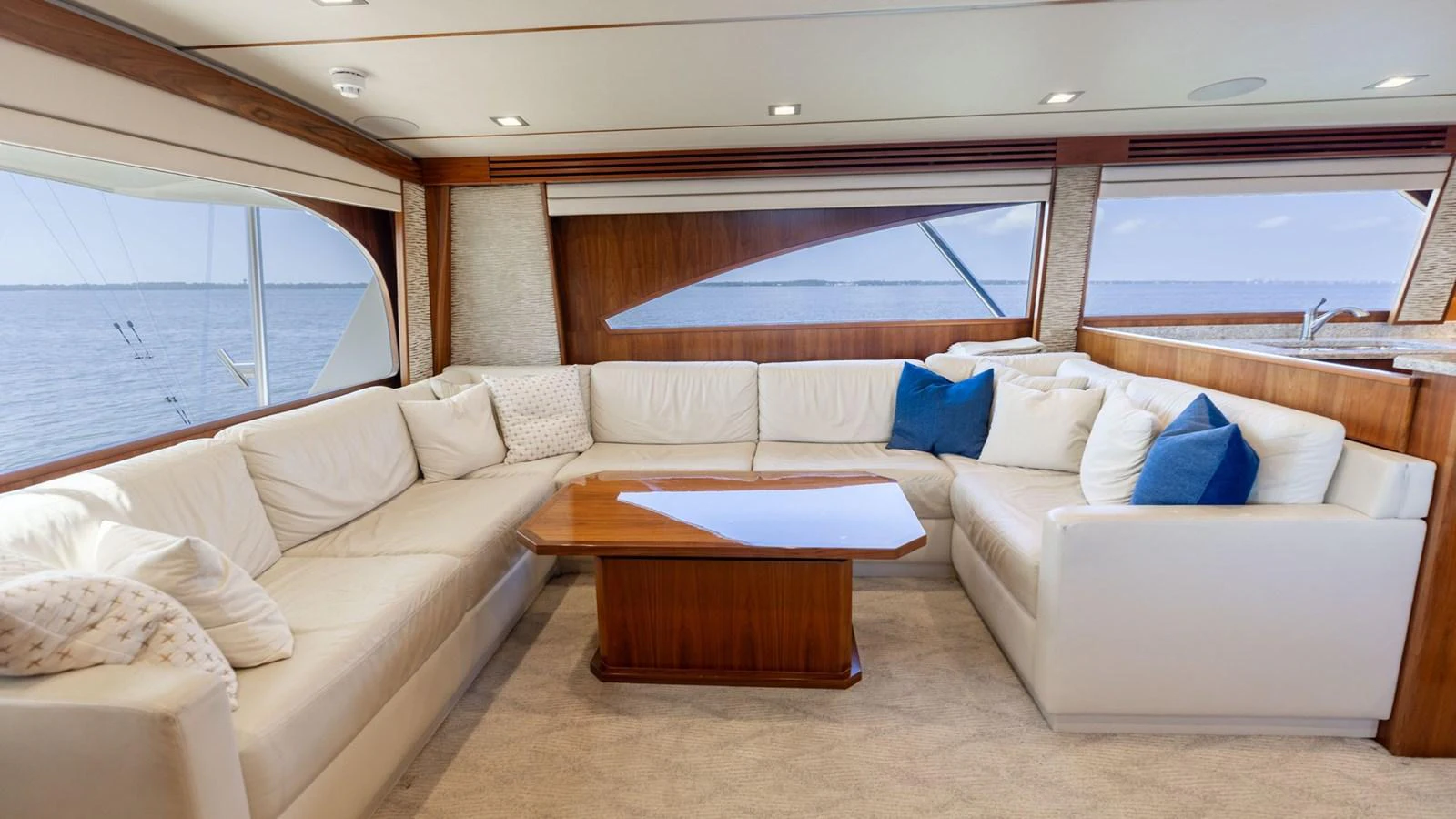 The salon features a spacious seating area with plush white sofas and a wooden coffee table, offering panoramic views through large windows. aboard CE Yacht for Sale