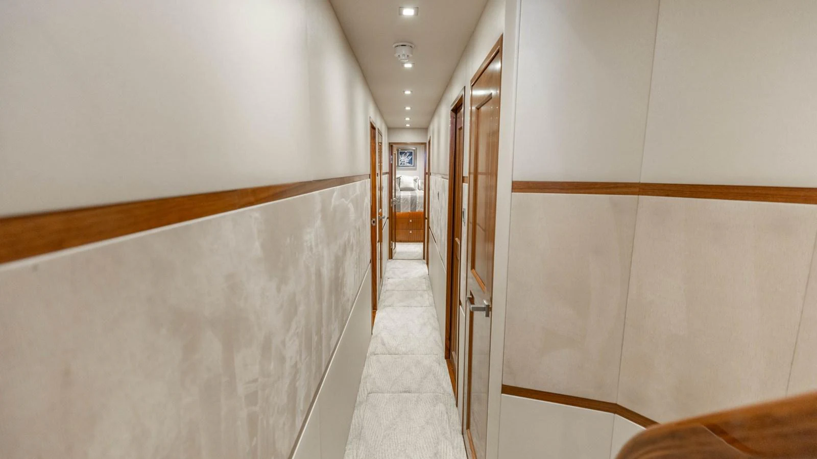 A well-lit hallway with wooden accents and plush carpeting leads to the yacht's staterooms. aboard CE Yacht for Sale