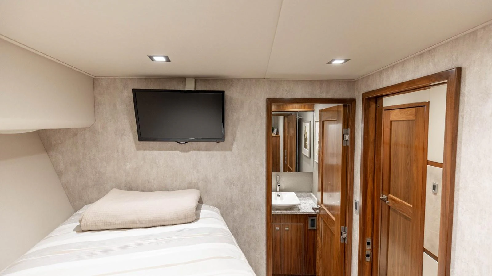 The guest stateroom features a cozy bed, a wall-mounted TV, and an ensuite bathroom. aboard CE Yacht for Sale