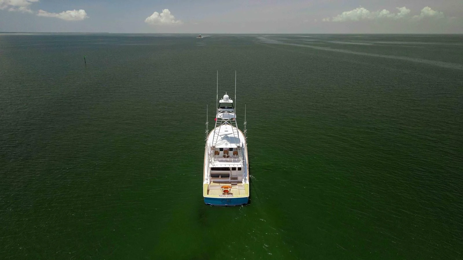 A yacht is seen from the rear, cruising on calm waters under a clear sky. aboard CE Yacht for Sale