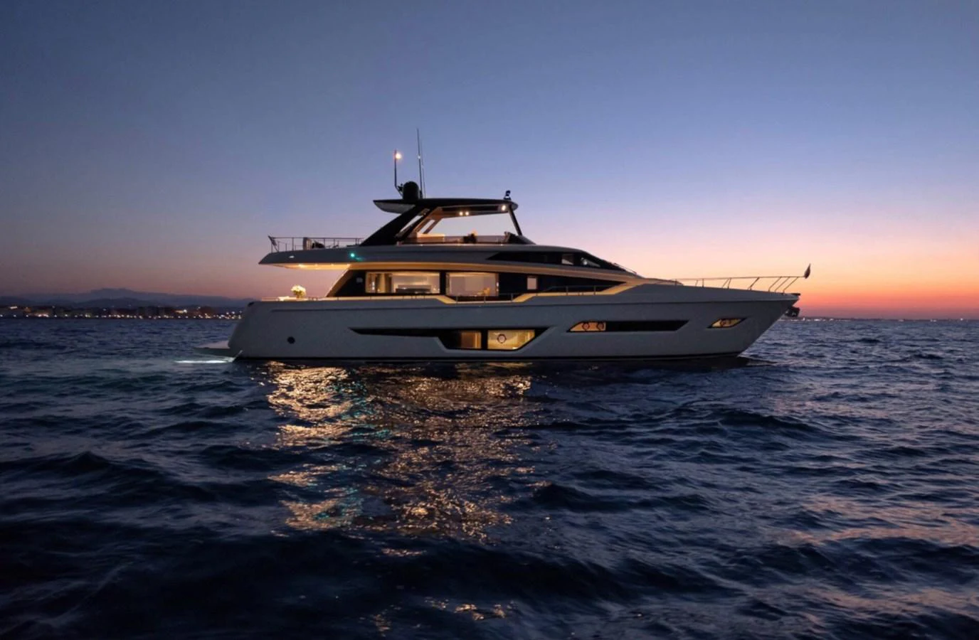 A sleek yacht cruises at dusk, illuminated against the twilight sky. aboard LD Yacht for Sale