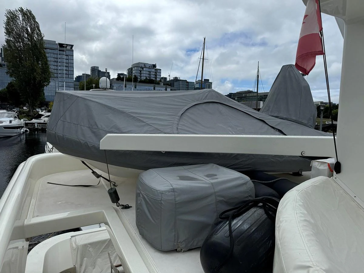 The image shows a covered tender on the deck of a yacht, with a cityscape in the background. aboard SHOW ME THE MONEY Yacht for Sale