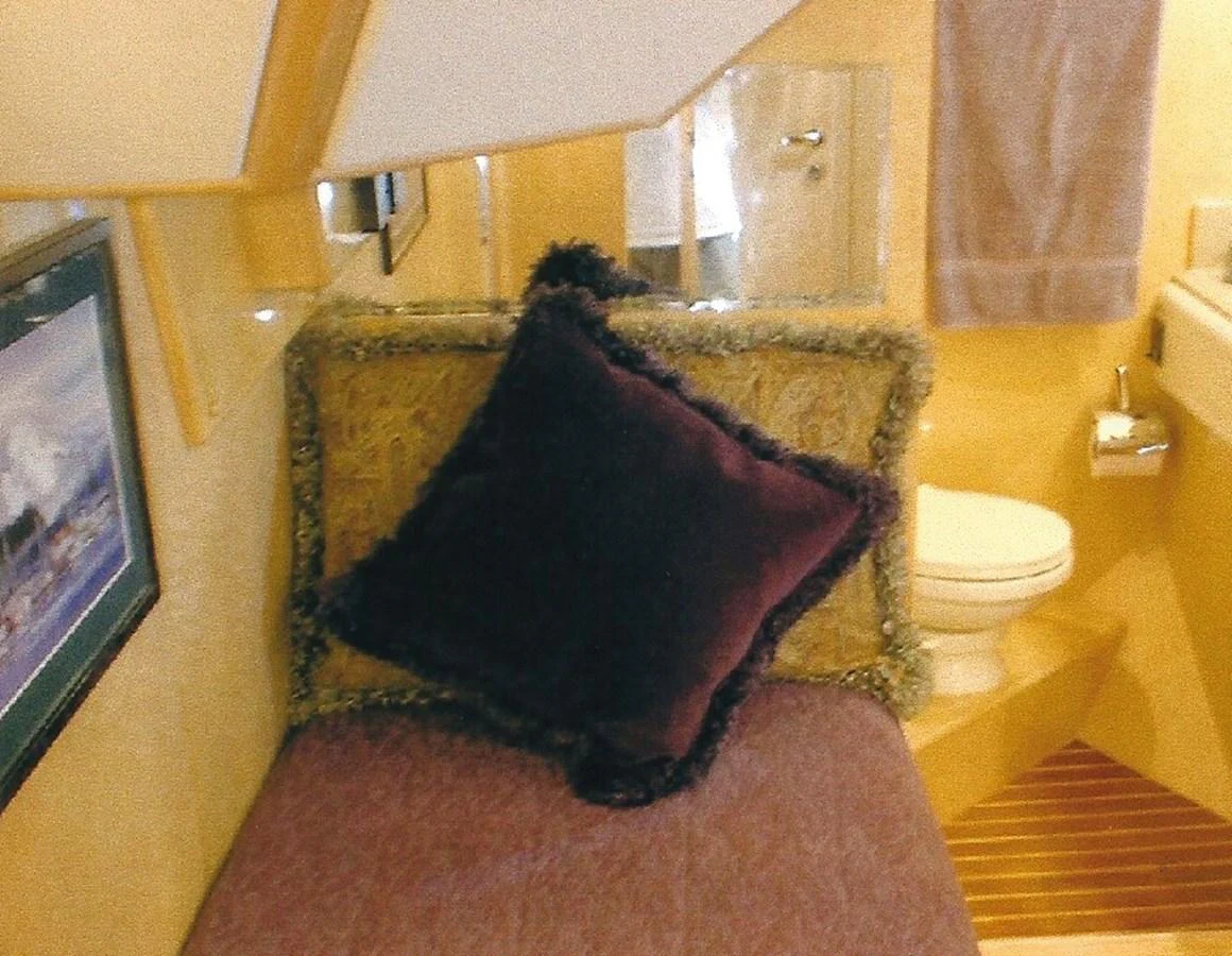 A cozy interior space featuring a cushioned seating area with a plush pillow and a nearby bathroom. aboard SHOW ME THE MONEY Yacht for Sale