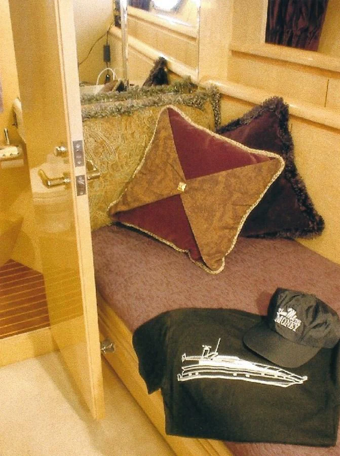 A cozy interior space featuring a cushioned seating area adorned with decorative pillows and a yacht-themed cap and shirt. aboard SHOW ME THE MONEY Yacht for Sale