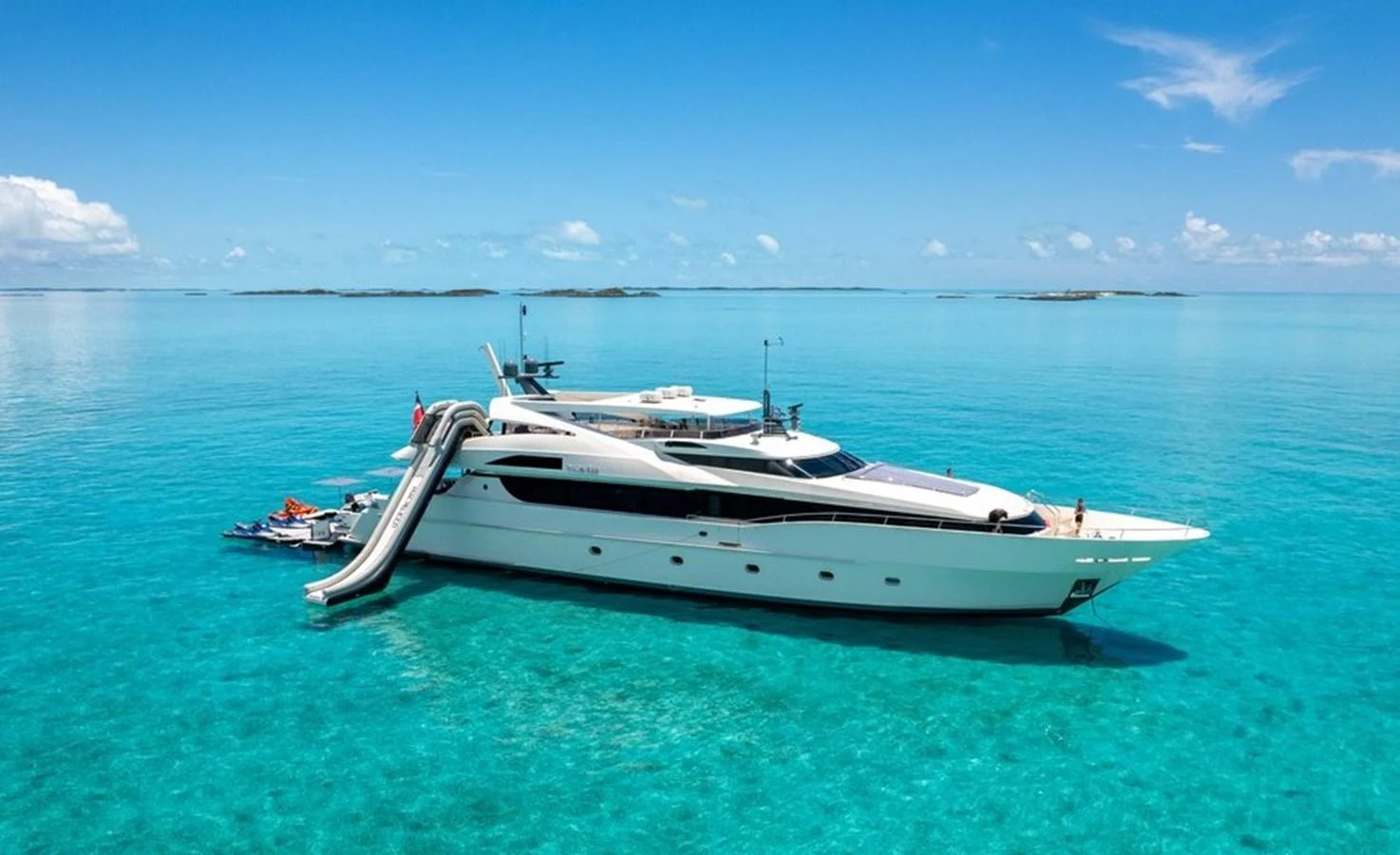 A sleek yacht is anchored in crystal-clear turquoise waters under a bright blue sky. aboard BLACK SHEEP Yacht for Sale