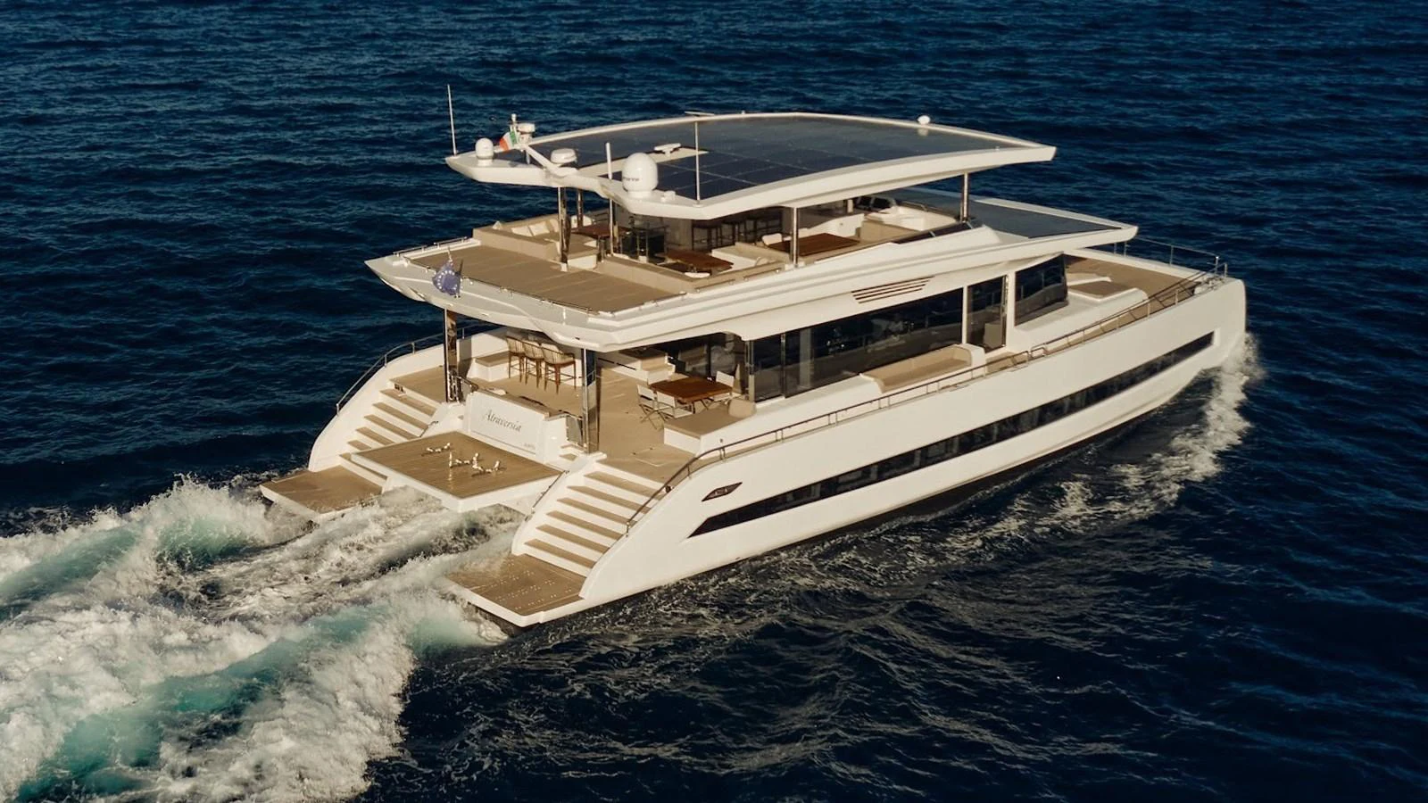 A luxurious multi-deck yacht cruising through the open sea, showcasing its sleek design and spacious outdoor areas. aboard ATRAVERSIA Yacht for Sale