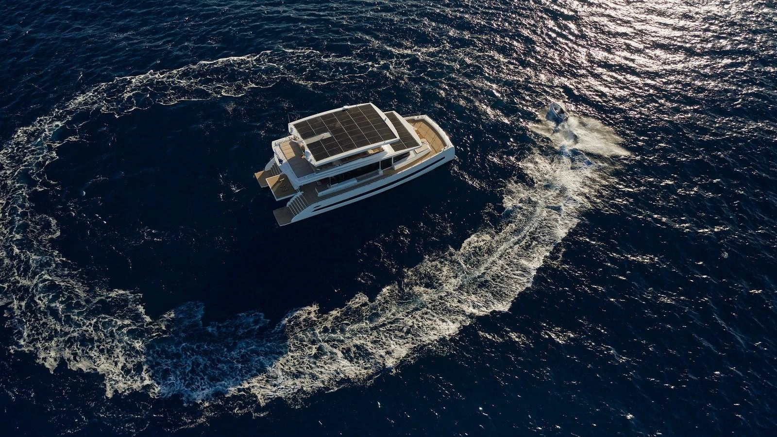 A sleek yacht navigates through the open sea, leaving a circular wake behind. aboard ATRAVERSIA Yacht for Sale