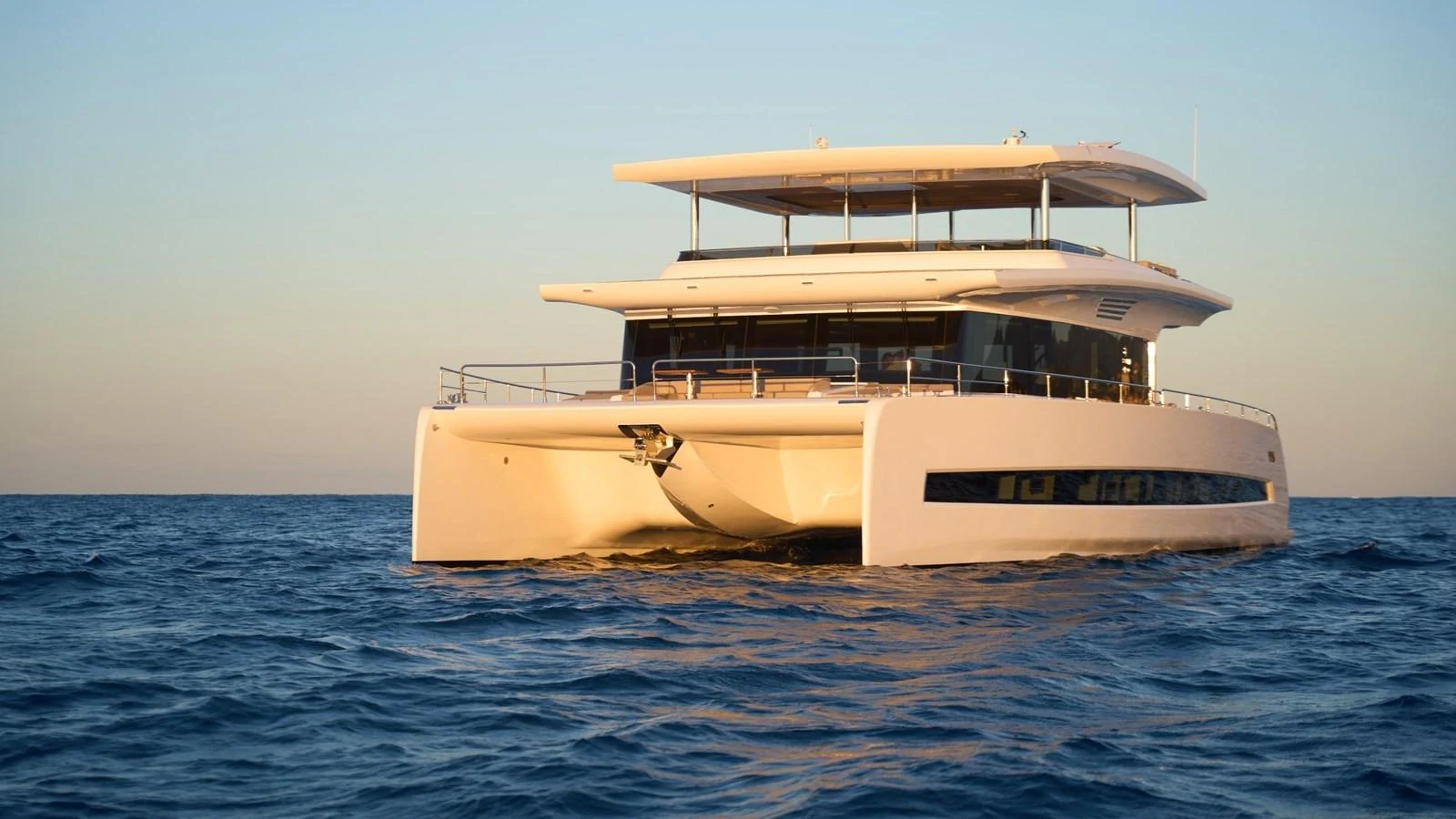 A luxurious catamaran yacht cruising on calm waters at sunset. aboard ATRAVERSIA Yacht for Sale