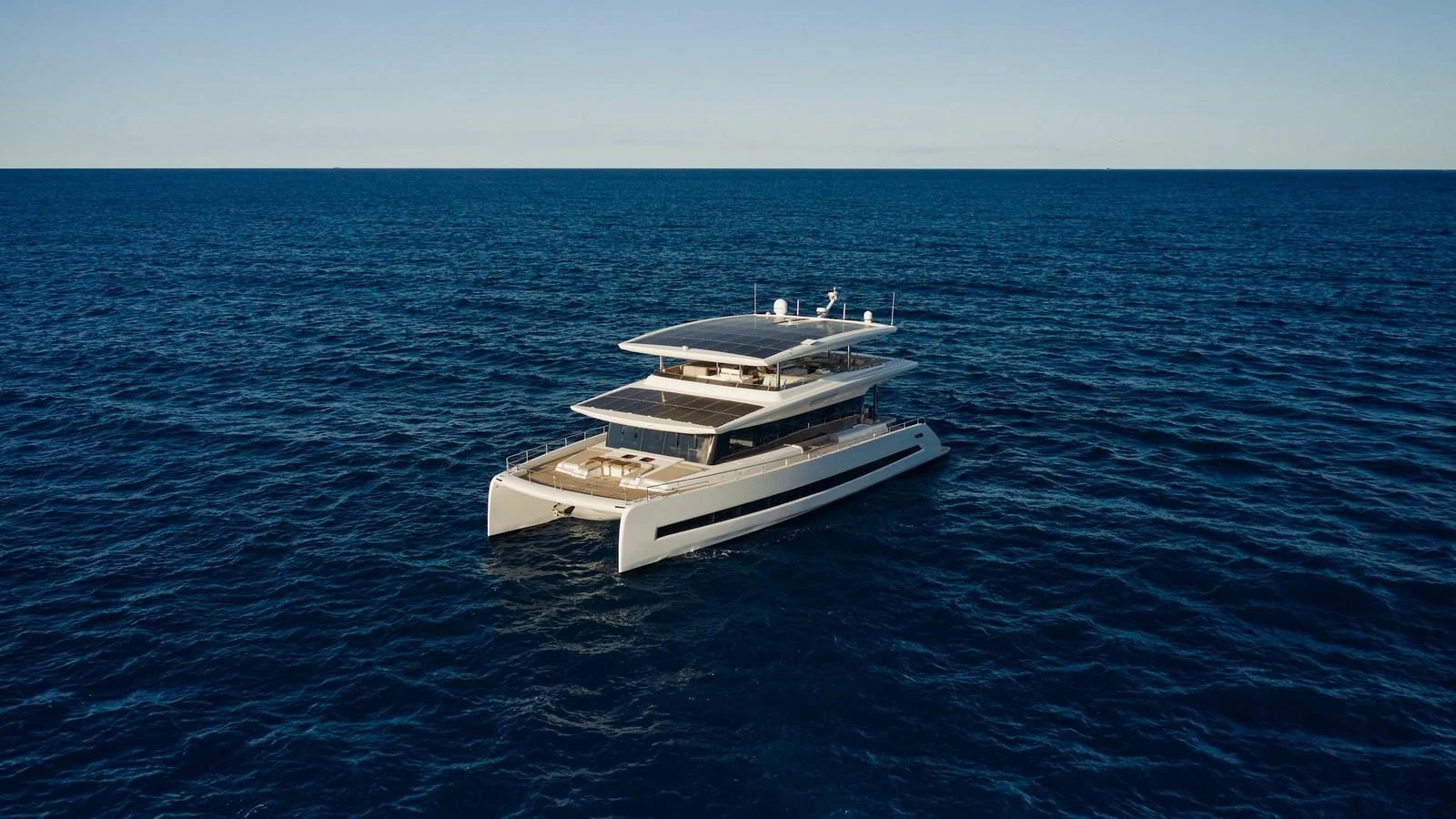 A sleek, modern yacht cruises through the open sea under a clear sky. aboard ATRAVERSIA Yacht for Sale