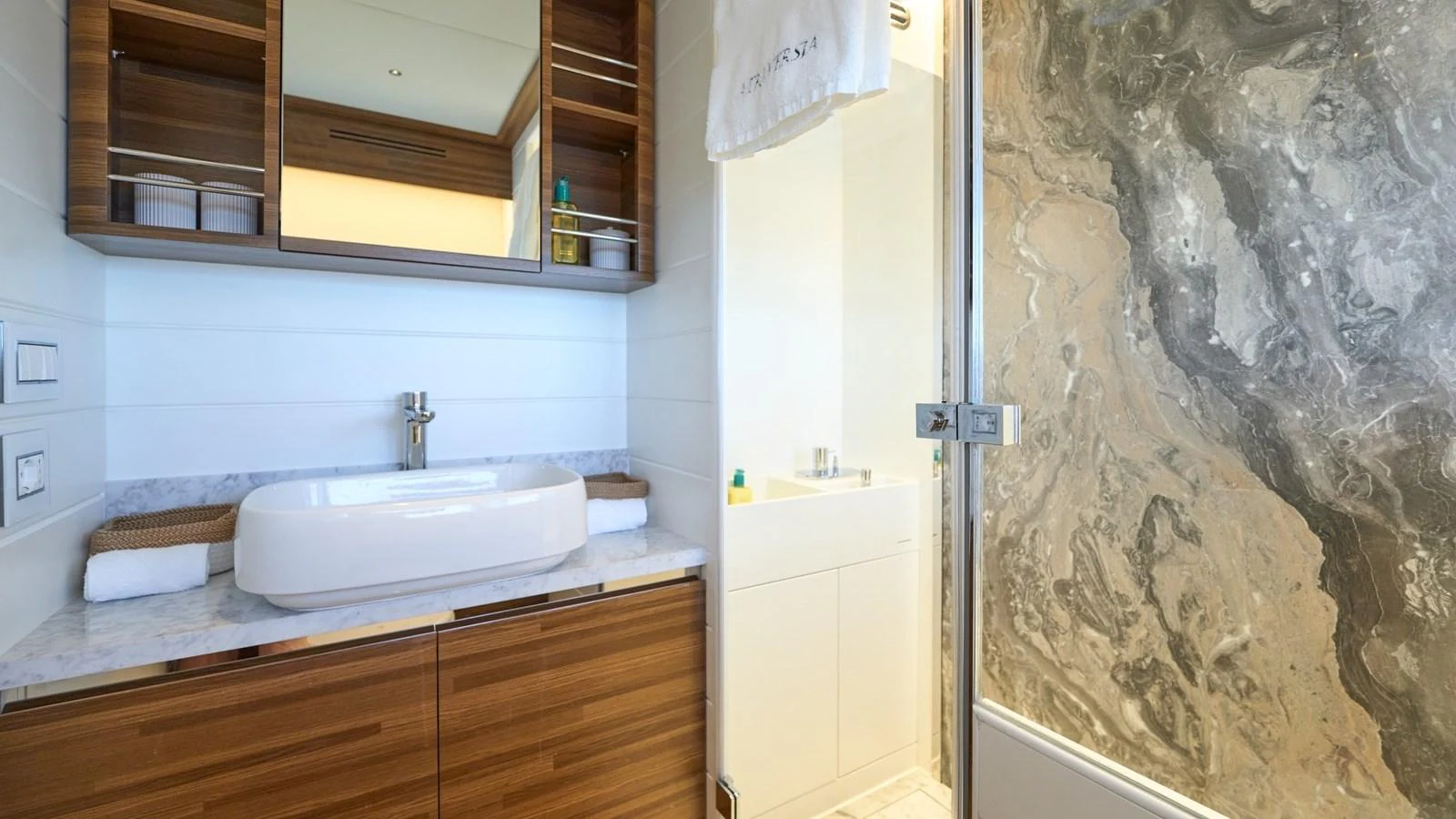 A luxurious yacht bathroom featuring a modern sink, wooden cabinetry, and a spacious shower with a marble wall. aboard ATRAVERSIA Yacht for Sale