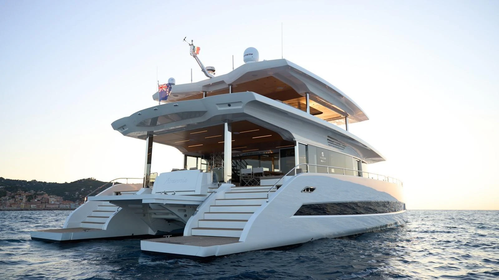 A luxurious catamaran yacht is anchored on calm waters at sunset, showcasing its sleek design and spacious aft deck. aboard ATRAVERSIA Yacht for Sale