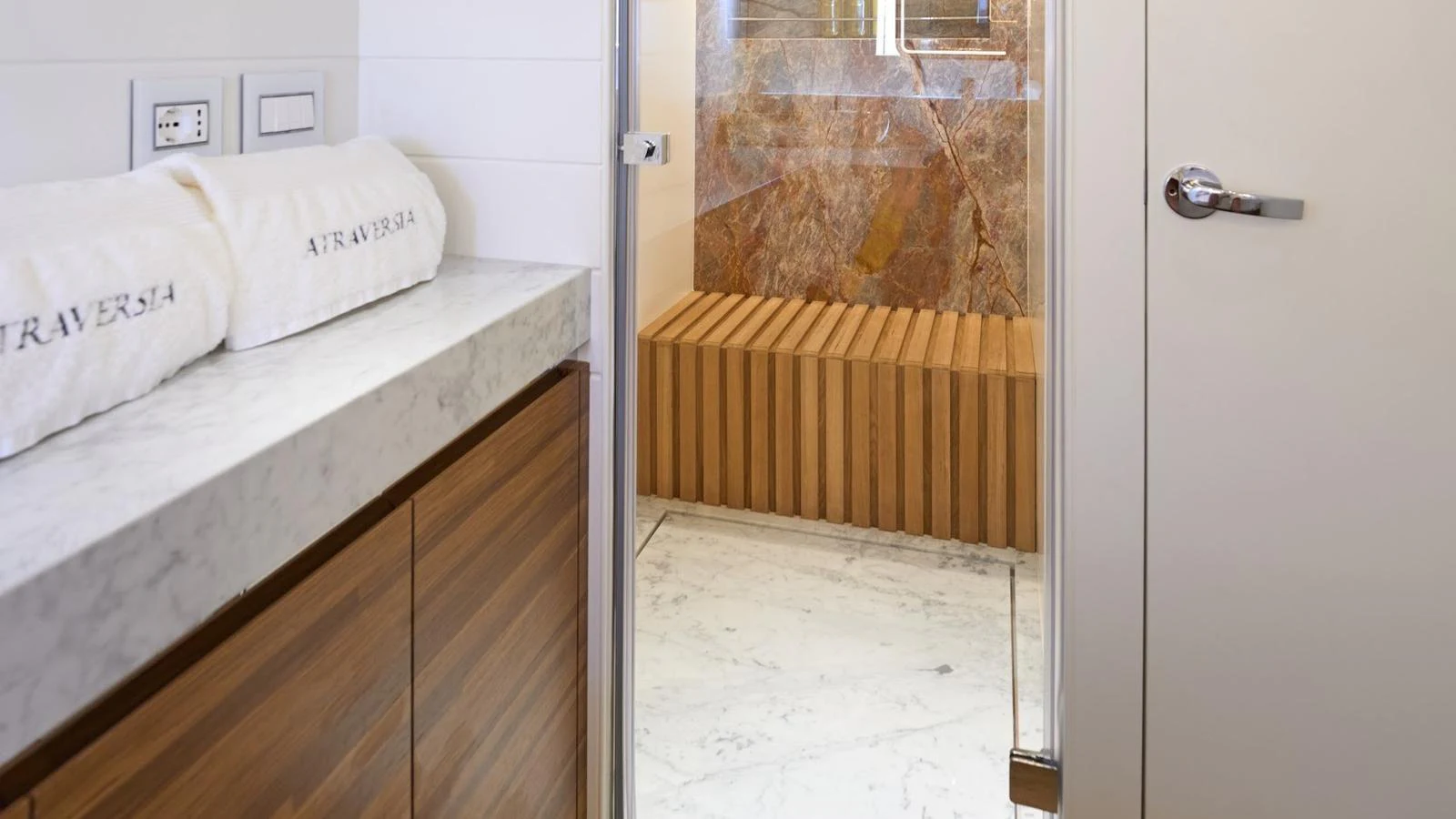 This image showcases a luxurious yacht bathroom with a marble countertop and a wooden bench in the shower area. aboard ATRAVERSIA Yacht for Sale