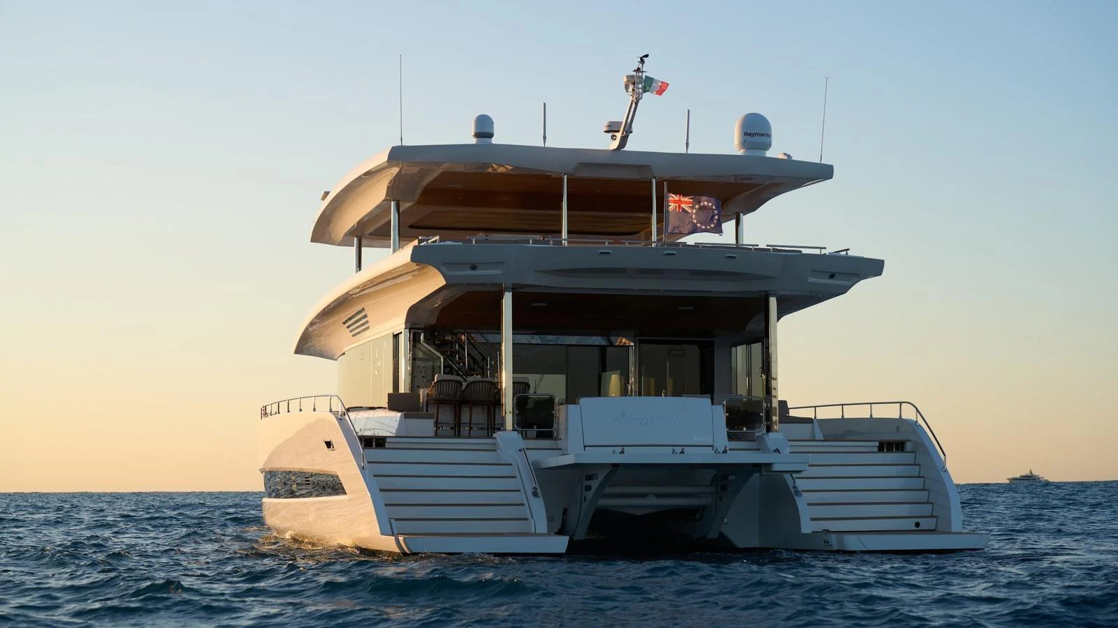 A luxurious catamaran yacht is seen from the rear, cruising on calm waters at sunset. aboard ATRAVERSIA Yacht for Sale