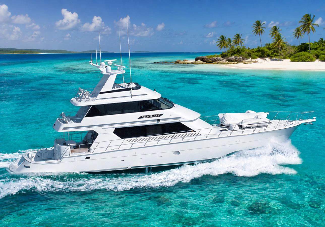 A sleek white yacht cruises through crystal-clear turquoise waters near a tropical island. aboard HATTERAS 92' Yacht for Sale