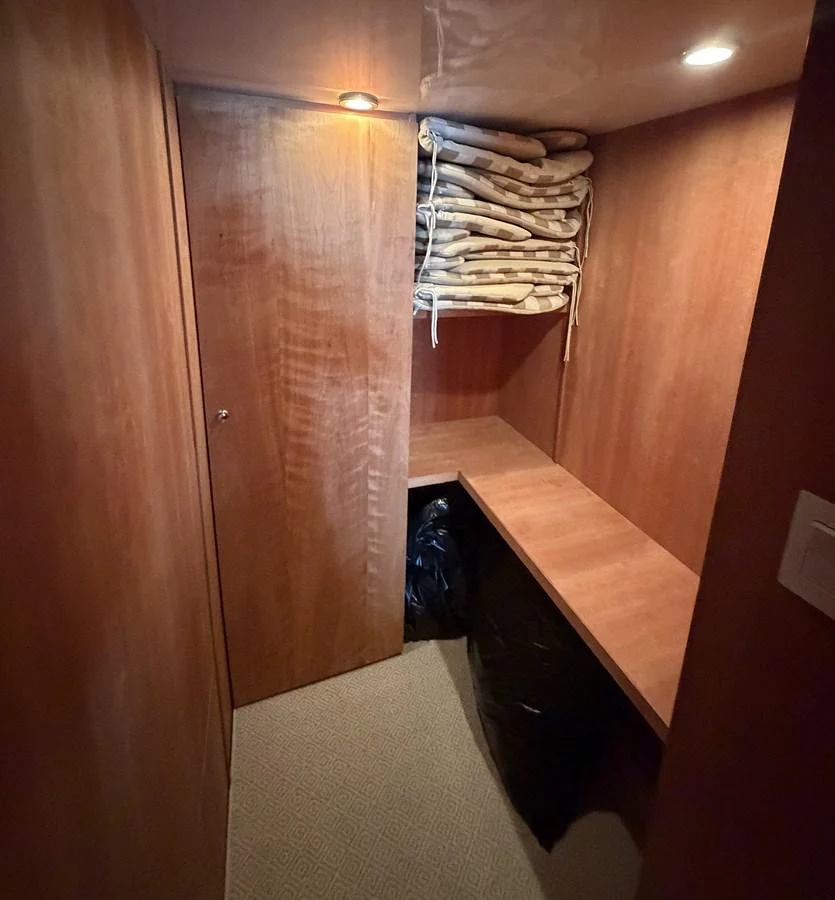 A compact storage area with wooden walls and shelves, featuring neatly stacked cushions. aboard HATTERAS 92' Yacht for Sale