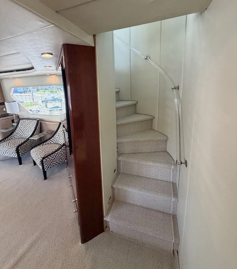 A stylish interior staircase leads to the upper deck, complemented by elegant seating and large windows. aboard HATTERAS 92' Yacht for Sale