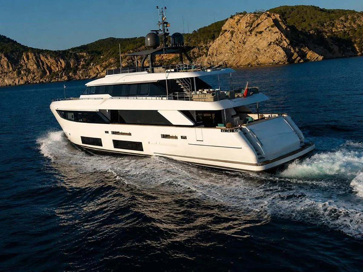A sleek and modern yacht cruises through the water with a scenic rocky coastline in the background. aboard ON Yacht for Sale