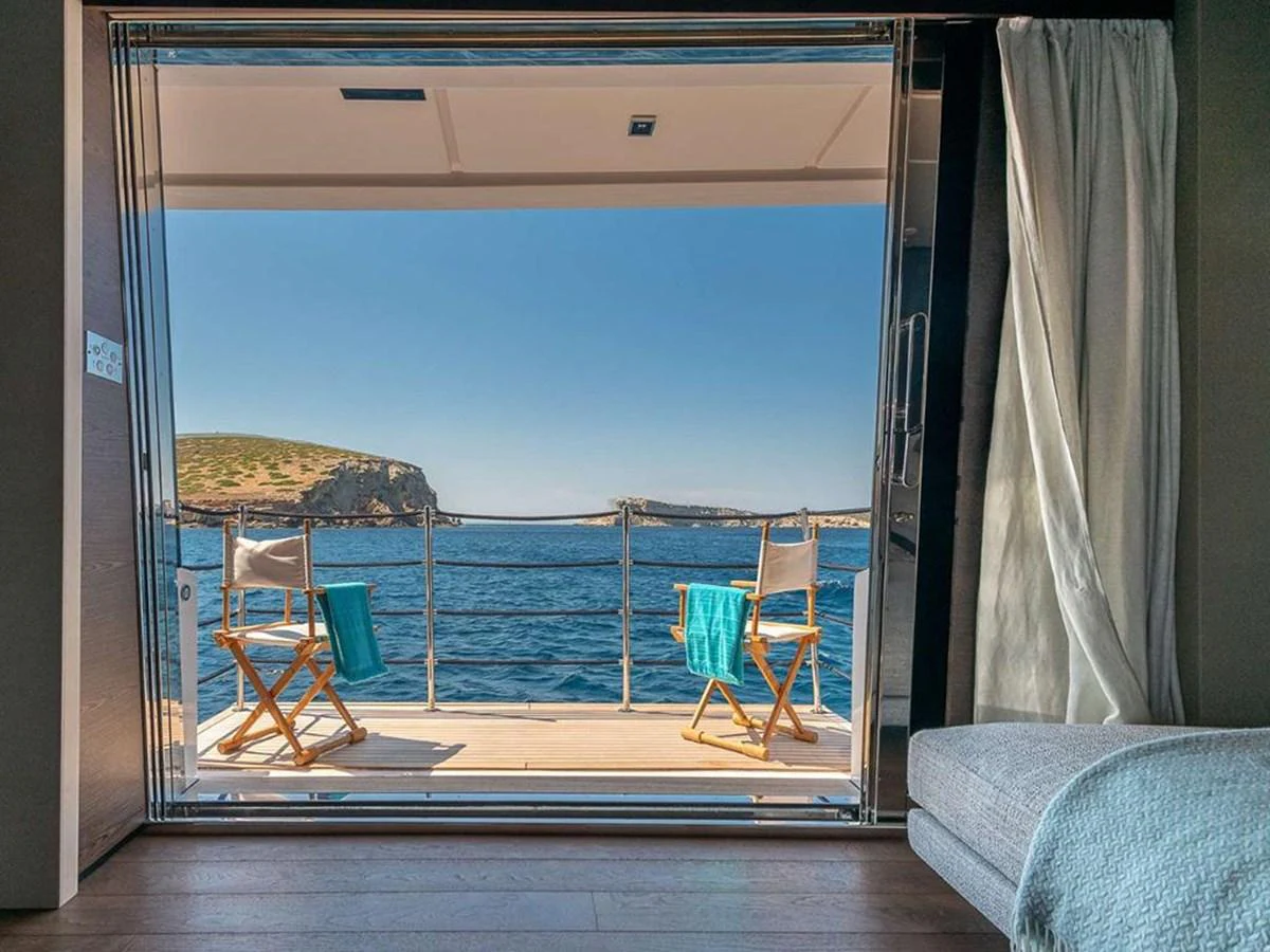 A serene view from a yacht's cabin opening onto a balcony with two chairs overlooking the sea. aboard ON Yacht for Sale
